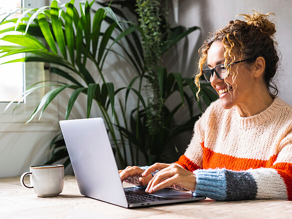 Happy woman writing on laptop on desk table in home office workplace. Adult female cheerful portrait wearing glasses and using laptop smiling. Modern alternative business job entrepreneur business, homeoffice